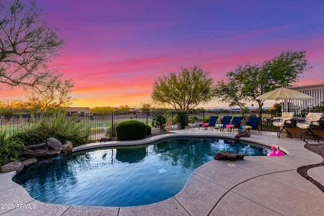 pool at dusk with a patio, fence, and a fenced in pool