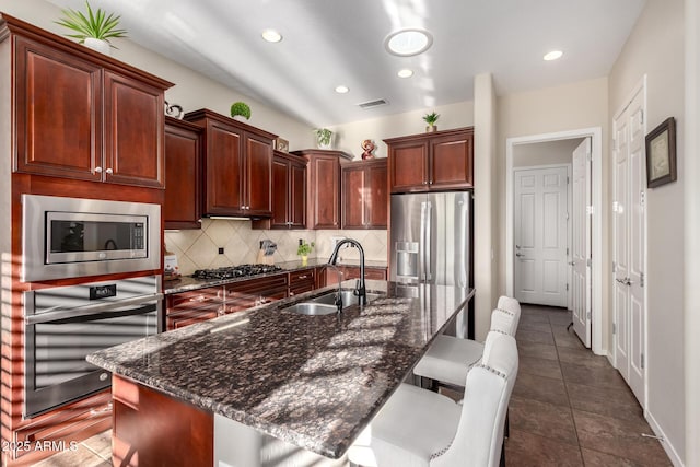 kitchen with backsplash, a kitchen bar, visible vents, a sink, and stainless steel appliances