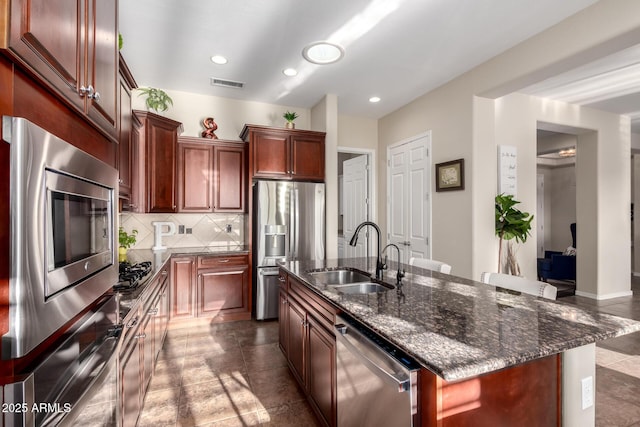 kitchen featuring decorative backsplash, visible vents, a center island with sink, a sink, and stainless steel appliances
