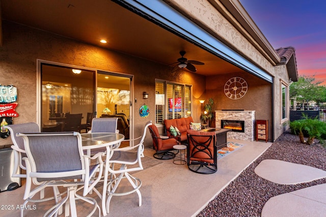patio terrace at dusk with an outdoor stone fireplace and ceiling fan