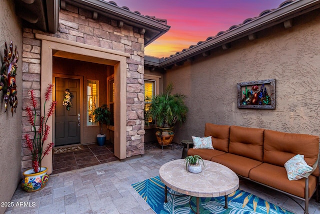 exterior entry at dusk with an outdoor living space, a patio area, stucco siding, and stone siding