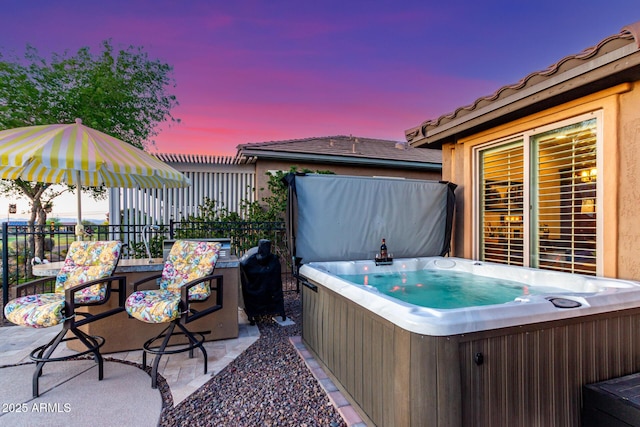 patio terrace at dusk featuring fence and a hot tub