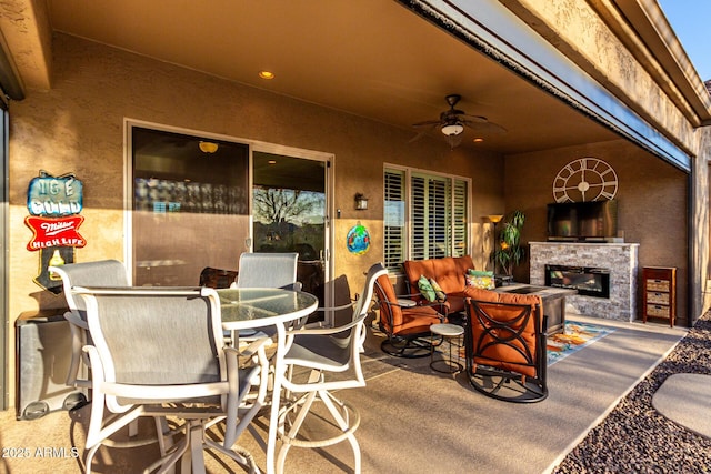 view of patio featuring a ceiling fan, outdoor dining space, and a glass covered fireplace