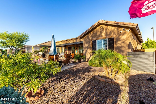 rear view of property with a patio, stucco siding, a tile roof, and fence