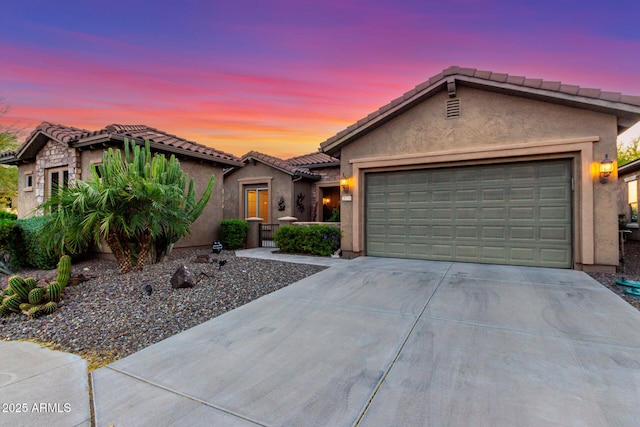 view of front facade featuring an attached garage, driveway, a tile roof, and stucco siding