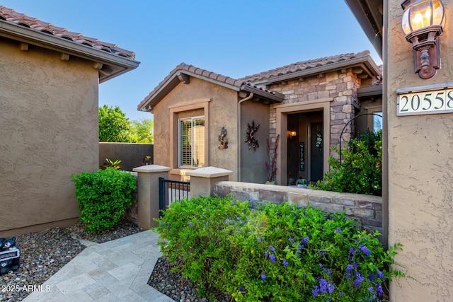 view of exterior entry with stucco siding, a tiled roof, and stone siding