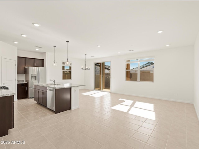 kitchen featuring pendant lighting, sink, appliances with stainless steel finishes, dark brown cabinetry, and light stone countertops