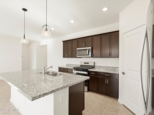 kitchen featuring decorative light fixtures, sink, light stone counters, stainless steel appliances, and a center island with sink