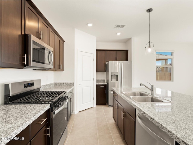 kitchen with dark brown cabinetry, sink, light stone counters, appliances with stainless steel finishes, and pendant lighting