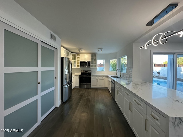 kitchen featuring kitchen peninsula, appliances with stainless steel finishes, white cabinets, light stone counters, and sink