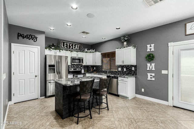 kitchen featuring light stone counters, stainless steel appliances, a kitchen island, white cabinetry, and a kitchen breakfast bar