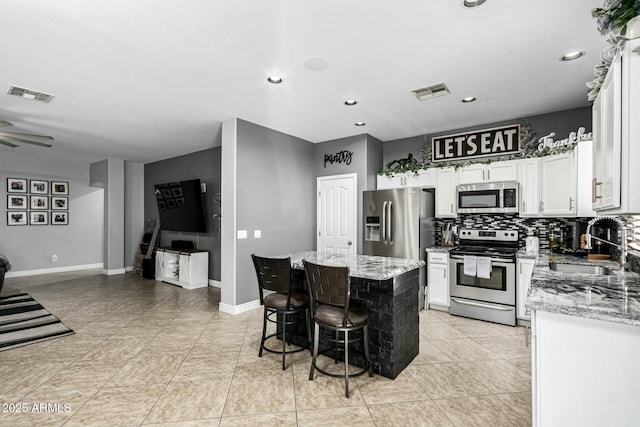 kitchen featuring sink, stainless steel appliances, light stone counters, and a center island