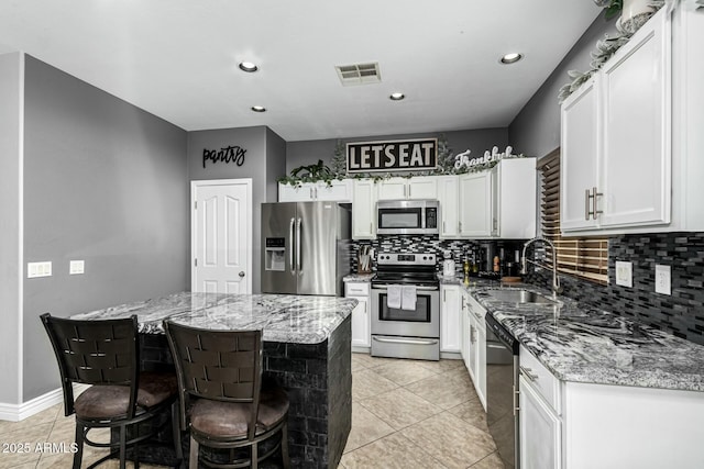 kitchen featuring light stone counters, light tile patterned floors, a kitchen island, white cabinetry, and appliances with stainless steel finishes