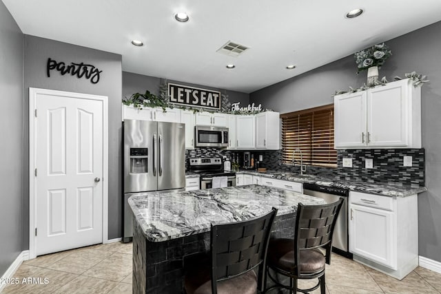 kitchen with sink, a center island, white cabinetry, light stone countertops, and appliances with stainless steel finishes