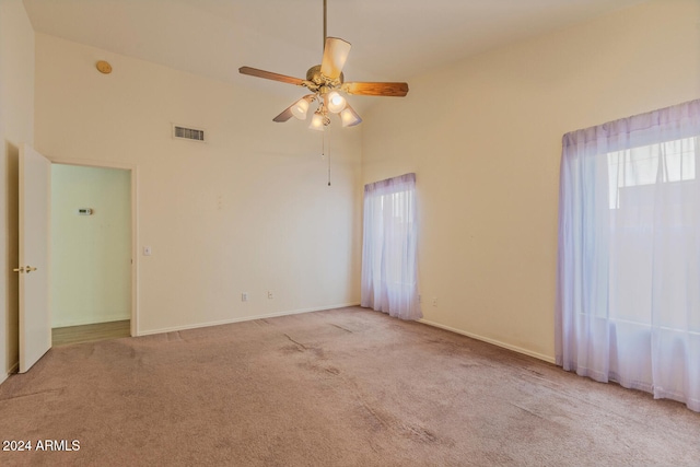 carpeted spare room with ceiling fan and a towering ceiling