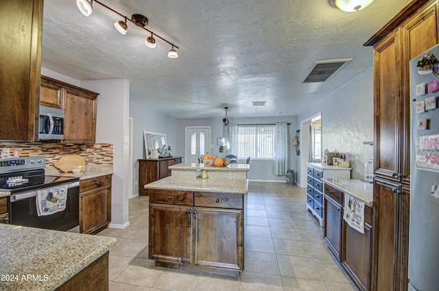 kitchen with hanging light fixtures, decorative backsplash, a textured ceiling, appliances with stainless steel finishes, and a kitchen island