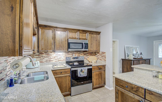 kitchen with light stone countertops, sink, stainless steel appliances, decorative backsplash, and light tile patterned flooring