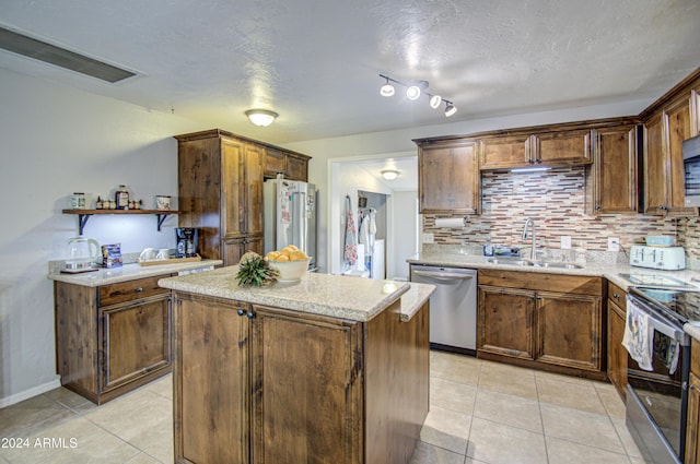 kitchen featuring backsplash, light stone counters, stainless steel appliances, sink, and a kitchen island