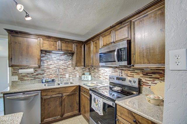 kitchen featuring sink, tasteful backsplash, light stone counters, light tile patterned floors, and appliances with stainless steel finishes