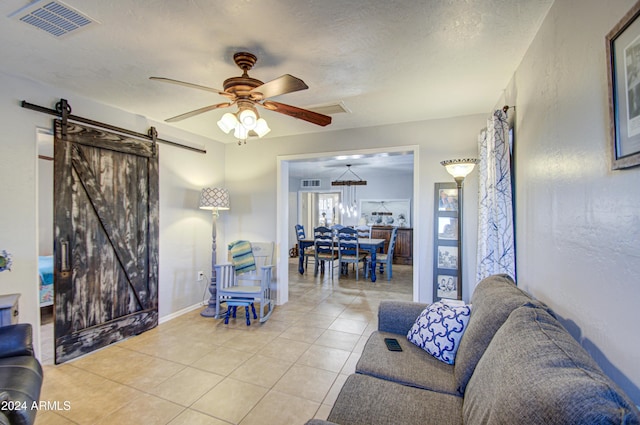 tiled living room featuring a textured ceiling, a barn door, and ceiling fan