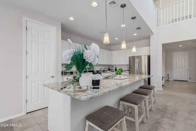 kitchen with a center island with sink, light stone counters, hanging light fixtures, white cabinets, and a kitchen bar