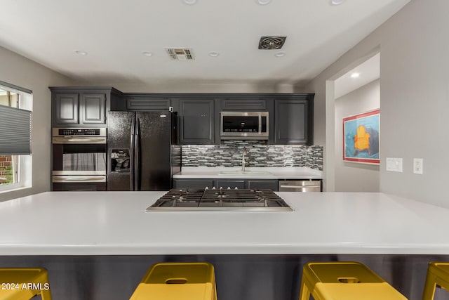 kitchen featuring decorative backsplash, sink, a breakfast bar area, appliances with stainless steel finishes, and kitchen peninsula