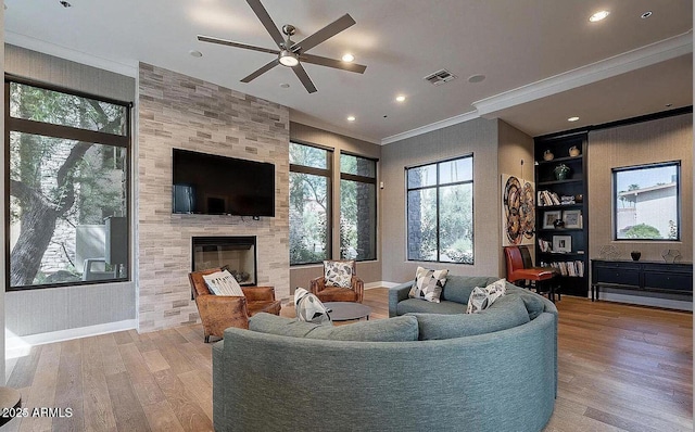 living area featuring visible vents, crown molding, a large fireplace, ceiling fan, and light wood-type flooring