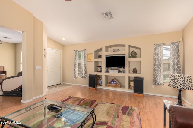 living room featuring vaulted ceiling, built in shelves, and light hardwood / wood-style floors