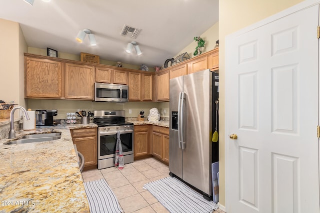 kitchen with appliances with stainless steel finishes, light tile patterned floors, light stone countertops, and sink