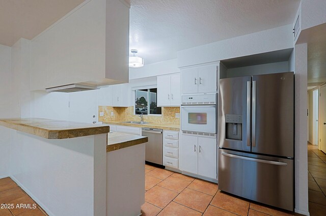 3054 W Redfield Rd, Phoenix, AZ 85053 - kitchen with appliances with stainless steel finishes, a peninsula, white cabinetry, a sink, and tasteful backsplash