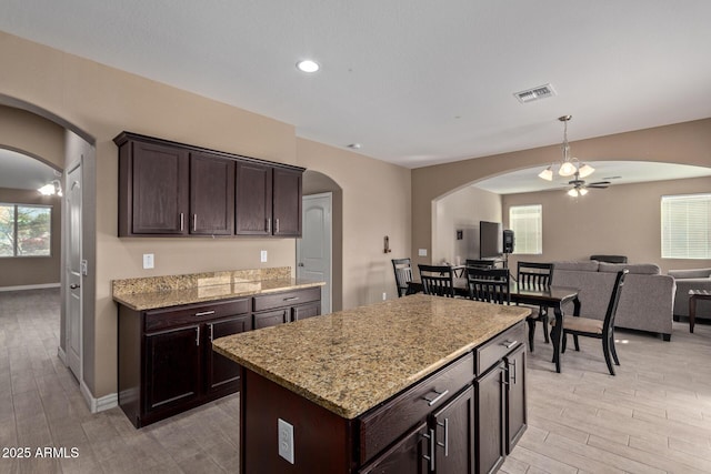 kitchen featuring ceiling fan, a center island, light stone counters, and dark brown cabinetry