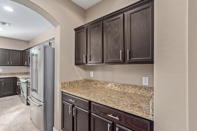 kitchen featuring light stone counters, dark brown cabinets, and stainless steel appliances