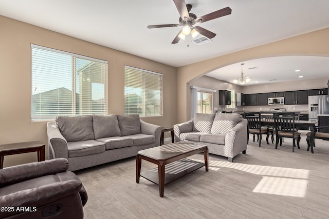 living room featuring ceiling fan with notable chandelier and light wood-type flooring