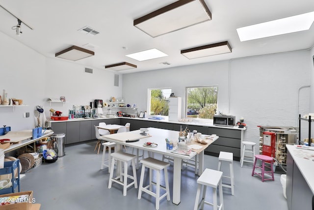 kitchen featuring gray cabinetry, a breakfast bar, rail lighting, and concrete flooring