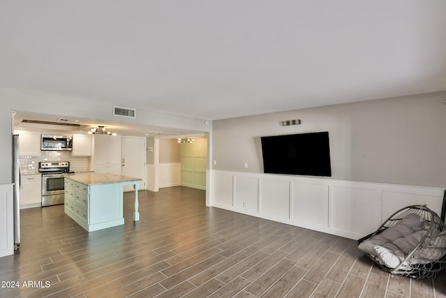 kitchen with decorative backsplash, stainless steel appliances, white cabinets, hardwood / wood-style floors, and a center island