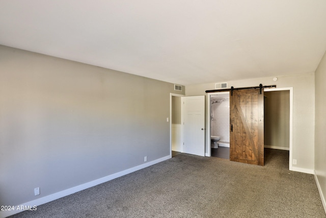 unfurnished bedroom with a barn door, connected bathroom, and dark carpet