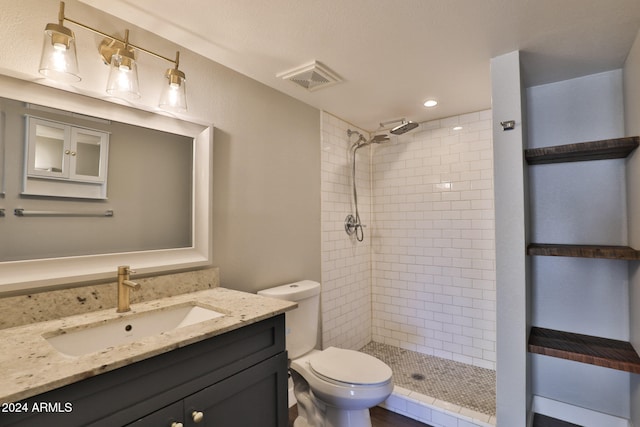 bathroom featuring a tile shower, vanity, and toilet