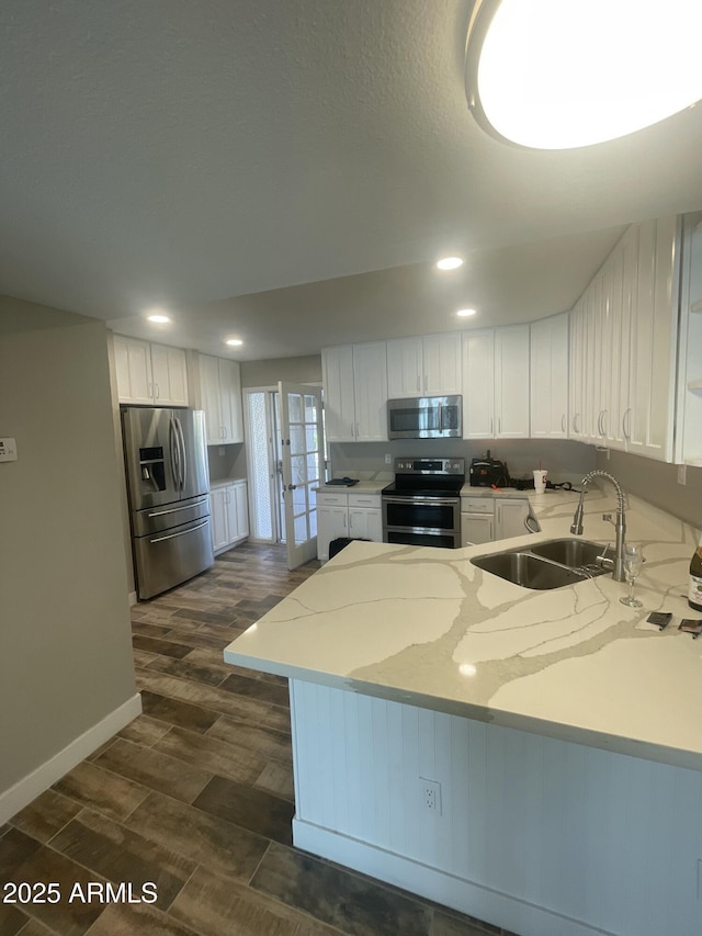 kitchen with light stone countertops, a peninsula, white cabinets, stainless steel appliances, and a sink