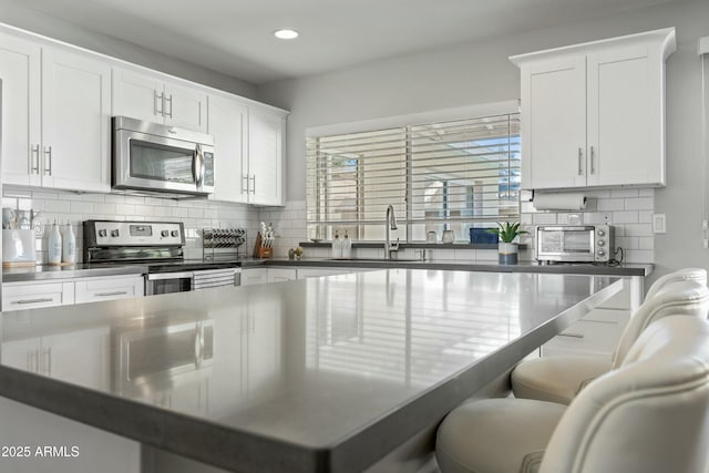 kitchen featuring tasteful backsplash, appliances with stainless steel finishes, a kitchen bar, and white cabinets