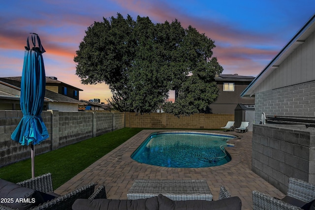 pool at dusk with a storage unit and a patio area