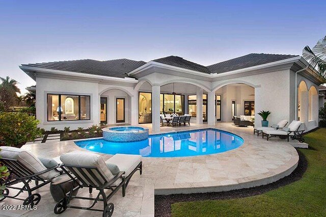 back house at dusk with a swimming pool with hot tub and a patio area