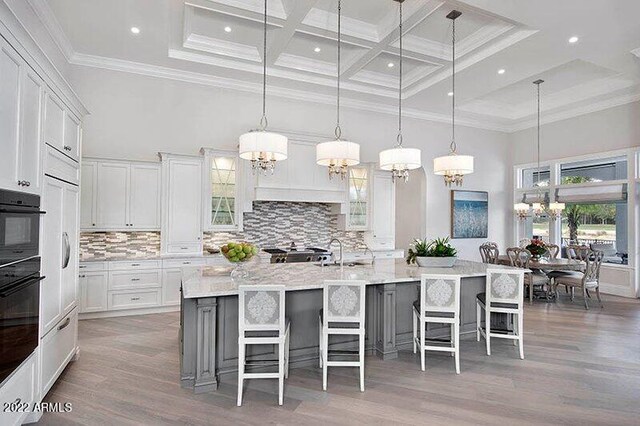 kitchen featuring a large island with sink, white cabinetry, a breakfast bar area, and decorative light fixtures