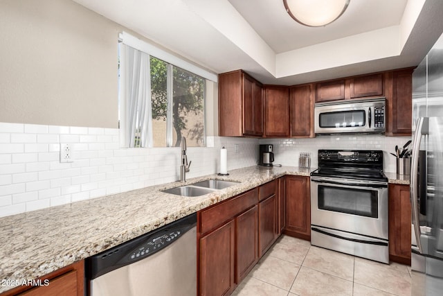 kitchen with stainless steel appliances, backsplash, a raised ceiling, a sink, and light stone counters