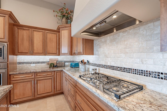 kitchen with custom range hood, appliances with stainless steel finishes, brown cabinetry, light tile patterned floors, and decorative backsplash