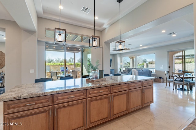 kitchen with visible vents, brown cabinets, pendant lighting, and light stone countertops