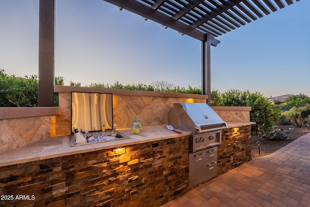 patio terrace at dusk with exterior kitchen, a pergola, and a grill