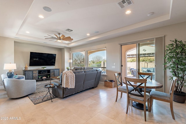 living room featuring a raised ceiling, visible vents, and a wealth of natural light