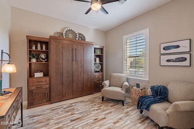 living area featuring light wood-style flooring, a ceiling fan, visible vents, and baseboards