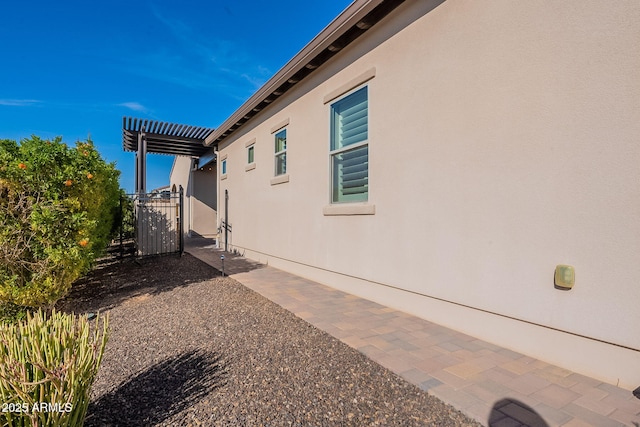 view of side of home with stucco siding and a gate