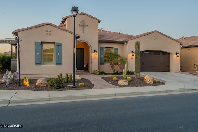 mediterranean / spanish home featuring stucco siding, concrete driveway, an attached garage, and a tiled roof